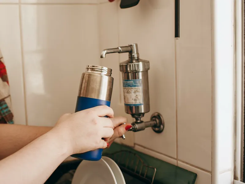 Filtro de água de parede em inox, com torneira, enchendo uma garrafa